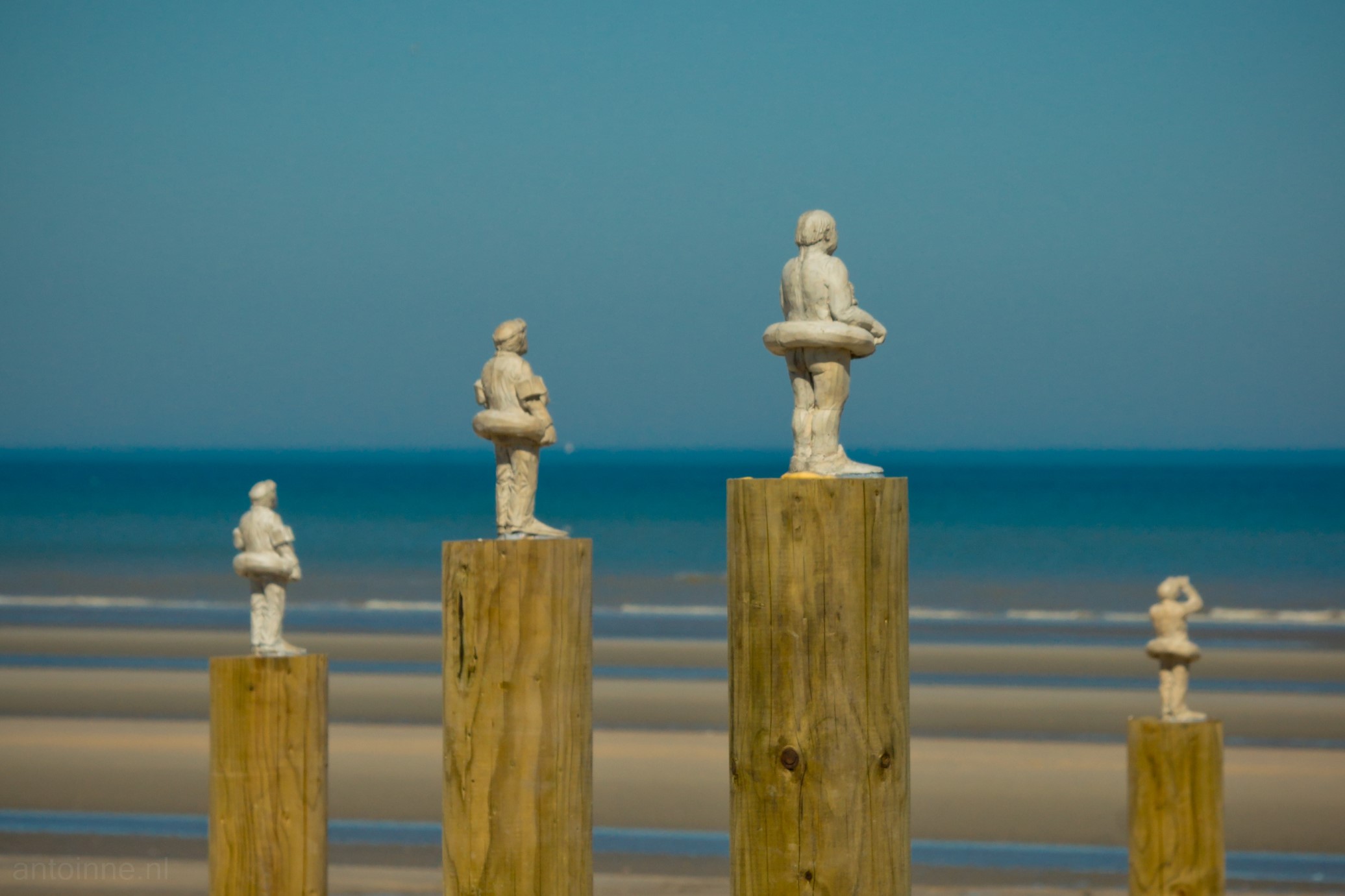 The photo shows a detail of an artwork called "Waiting for climate change" by Isaac Cordal. Small cement sculptures are watching the ocean on top of wooden poles. They are prepared with their mobile phones and diving equipment for an emergency. The artwork was on display in De Panne and was part of the BEAUFORT04 art trail on the Belgian coast in 2012.