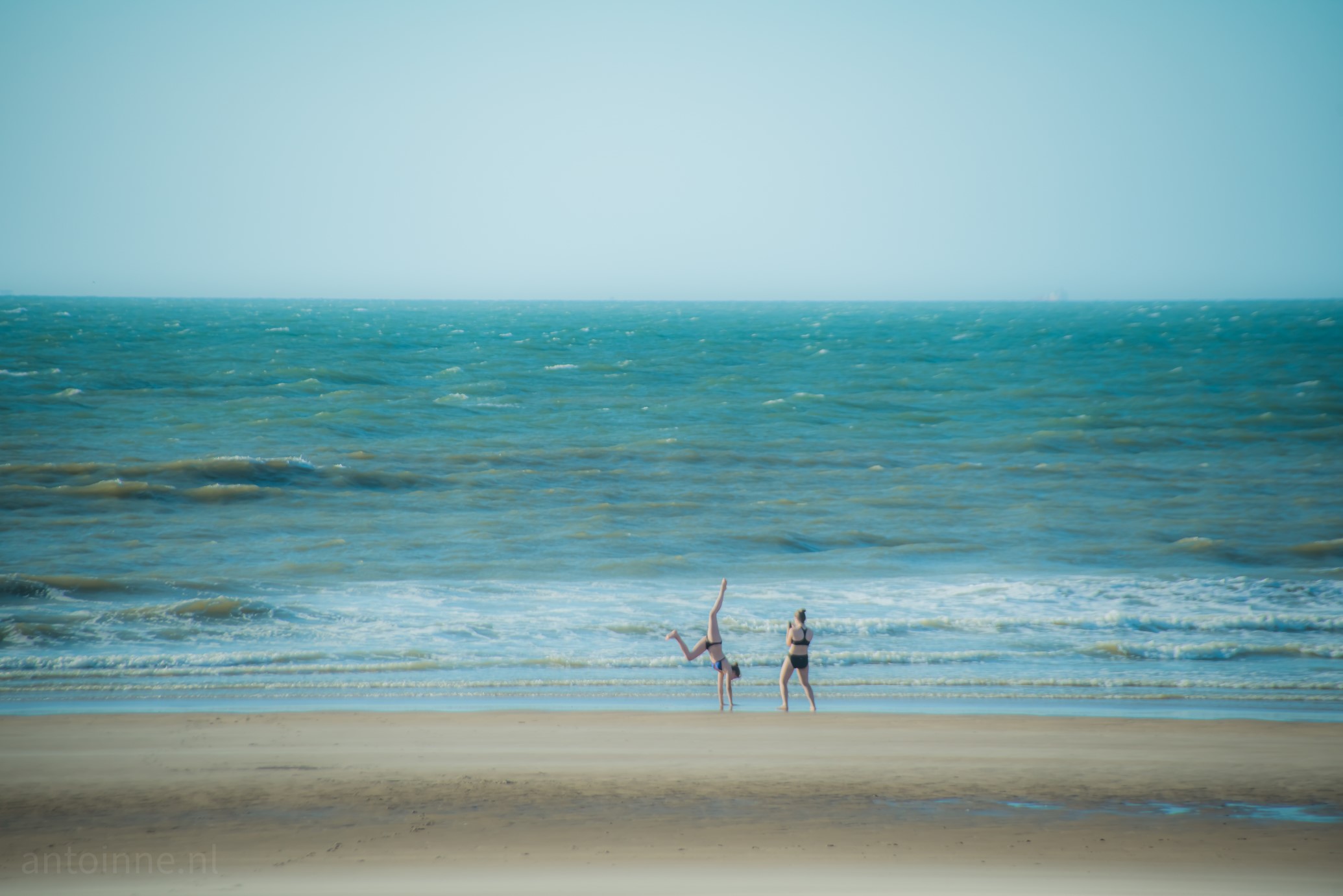 Two girls on the beach. One is doing cartwheels while the other takes pictures.
