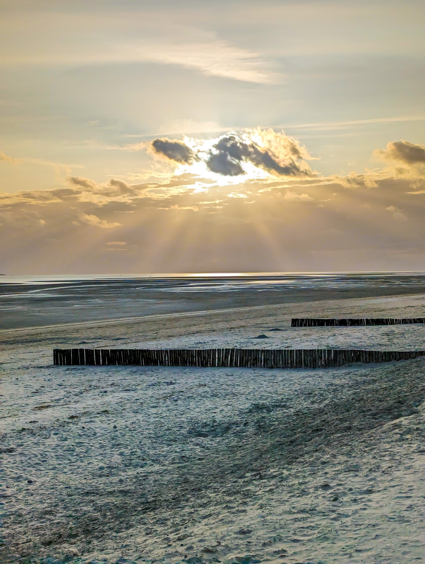 You are standing on the beach at Le Crotoy, France. In front of you there are two rows of wooden wave breakers. Behind them is France's largest estuary, the Bay of the Somme. It is low tide and the sand stretches out as far as the eye can see. The sun is setting. 