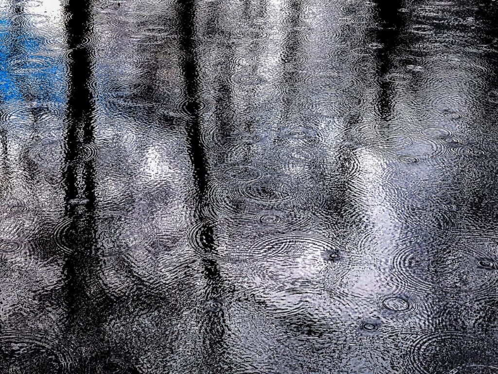 Raindrops are falling on the water. There is a hint of blue sky visible in the reflection